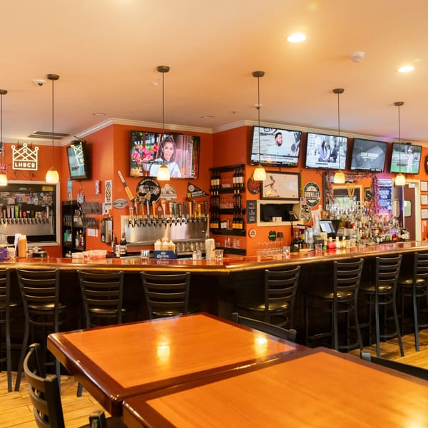 A lively bar interior with orange walls, multiple TVs, a long bar with stools, and beer taps.