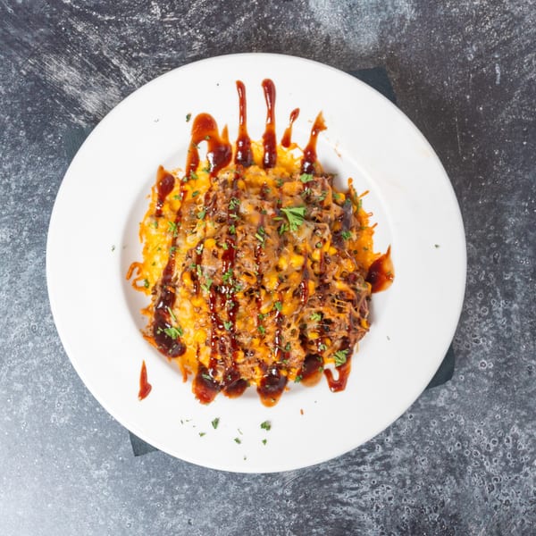 Pulled pork nachos with melted cheese, corn, and BBQ sauce, garnished with parsley on a white plate.