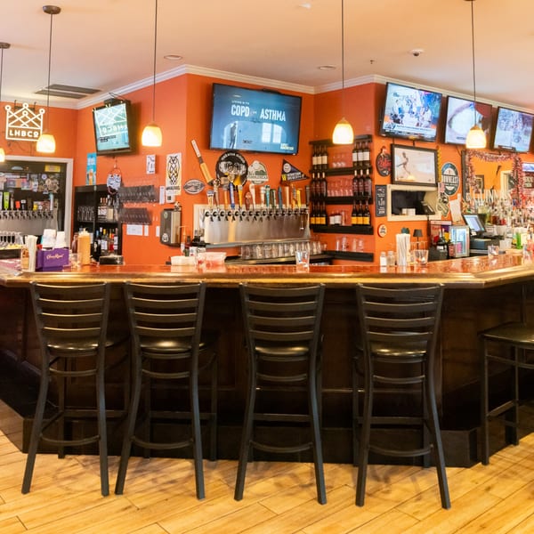 A vibrant bar with orange walls, multiple TVs, beer taps, and dark wooden bar stools.