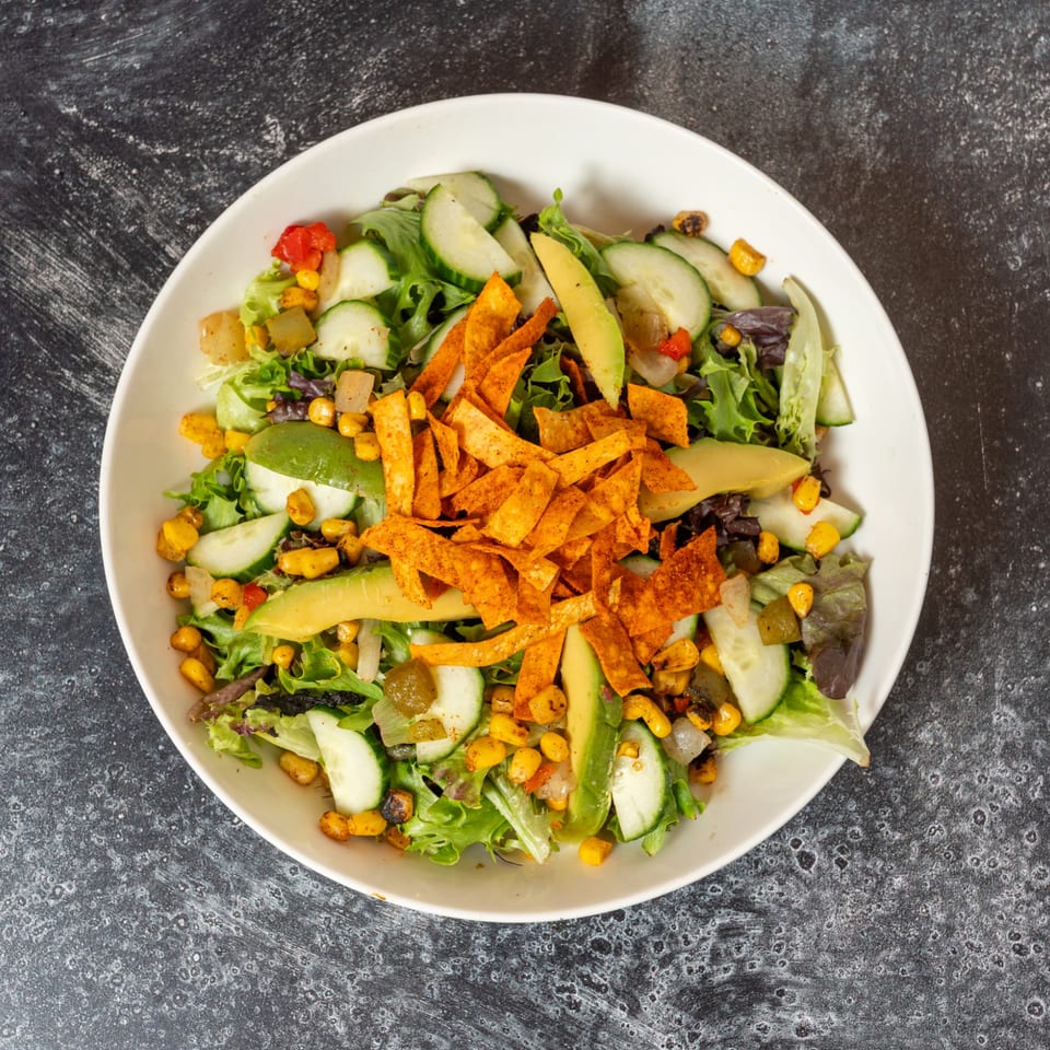 Overhead view of a vibrant salad with greens, cucumber, avocado, corn, and crispy tortilla strips.