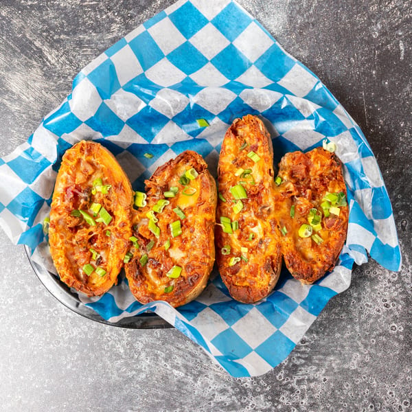 Four loaded potato skins with melted cheese and green onions in a blue and white checkered paper.