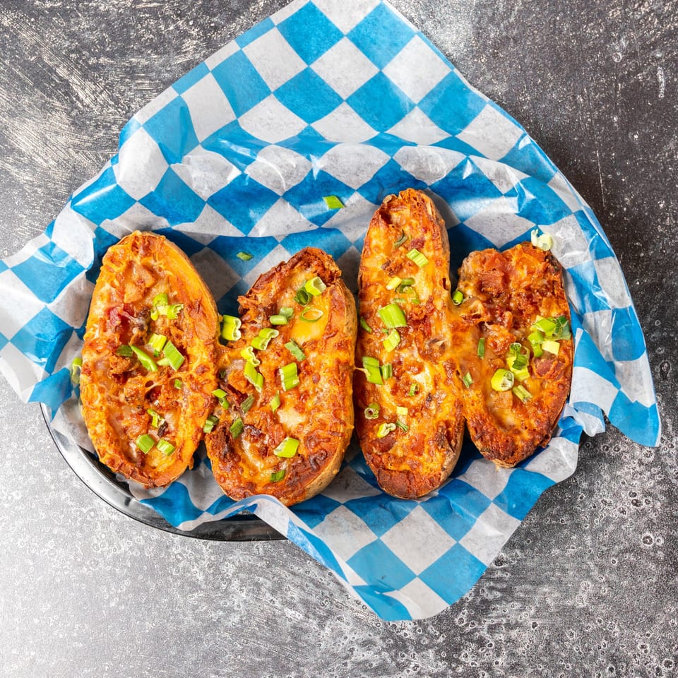Four loaded potato skins with melted cheese and green onions in a blue and white checkered paper.