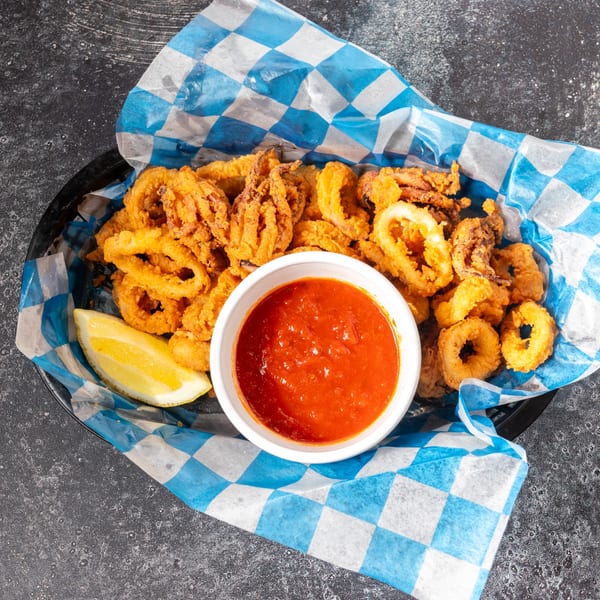 Crispy fried calamari rings and tentacles with a side of red marinara sauce and a lemon wedge.
