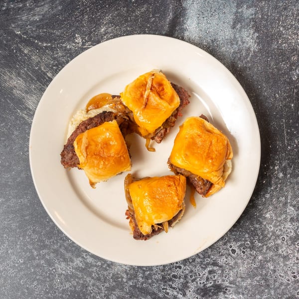 Four beef sliders with melted cheese and caramelized onions on a white plate.