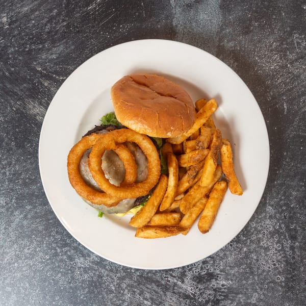 Overhead view of a burger with onion rings and fries on a white plate.