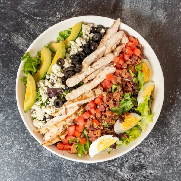Overhead view of a Cobb salad with grilled chicken, avocado, bacon, tomatoes, eggs, and olives.