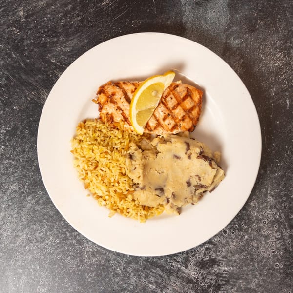 Grilled salmon with a lemon wedge, rice pilaf, and mashed potatoes on a white plate.