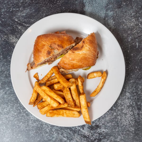 A Cuban sandwich cut in half, served with a side of golden french fries on a white plate.