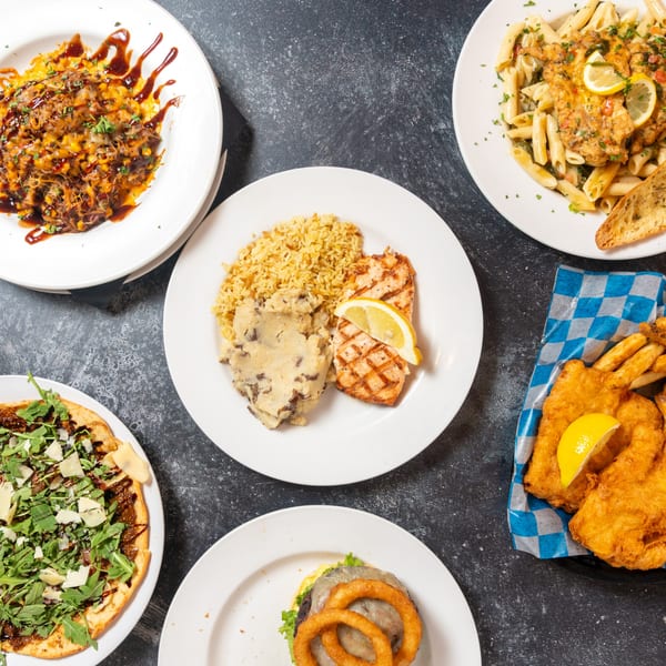 An overhead shot of five diverse dishes, including pasta, fish and chips, and a flatbread.
