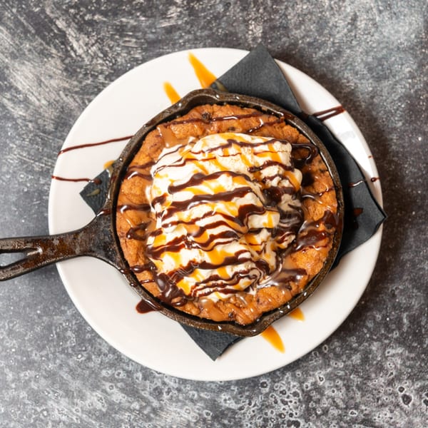 Skillet cookie with vanilla ice cream, chocolate, and caramel drizzle on a white plate.