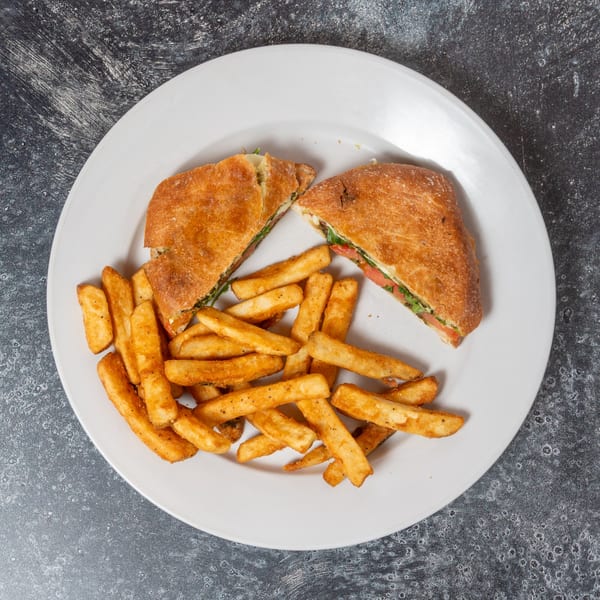 A panini sandwich cut in half with a side of french fries on a white plate.