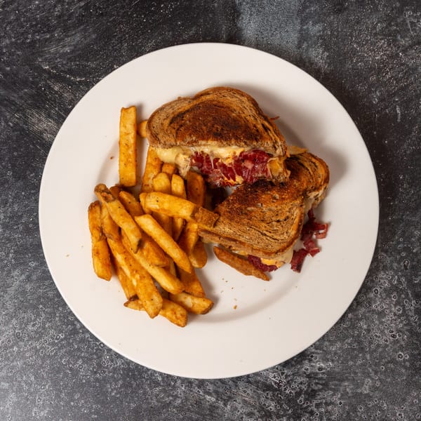 A grilled reuben sandwich with corned beef and melted cheese, served with a side of french fries.