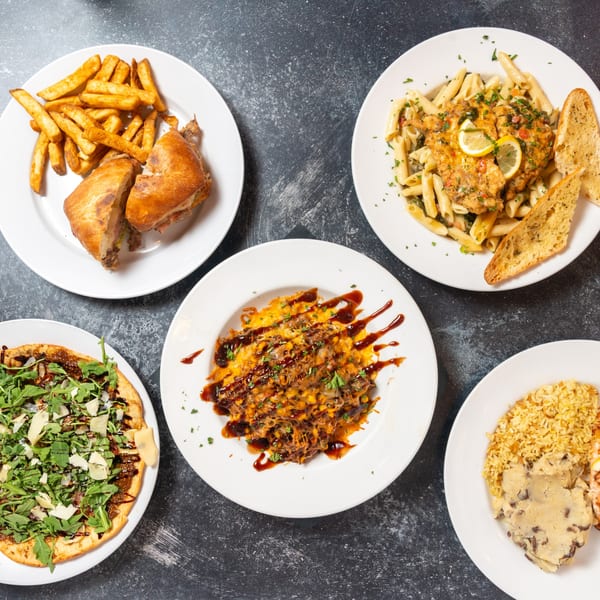 Five plates of diverse dishes, including pasta, fries, flatbread, and rice, arranged on a dark surface.