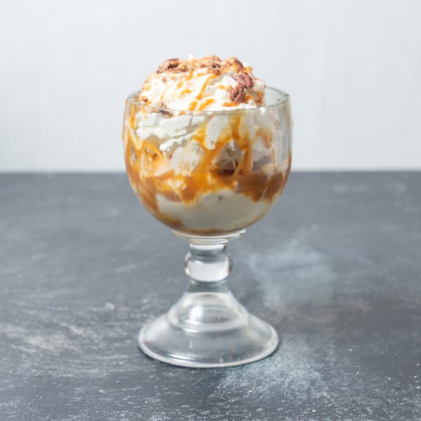 A glass goblet filled with ice cream, whipped cream, caramel drizzle, and chopped nuts.