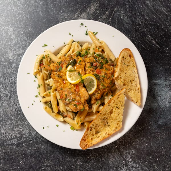 Chicken piccata with penne pasta, lemon slices, and garlic bread on a white plate.