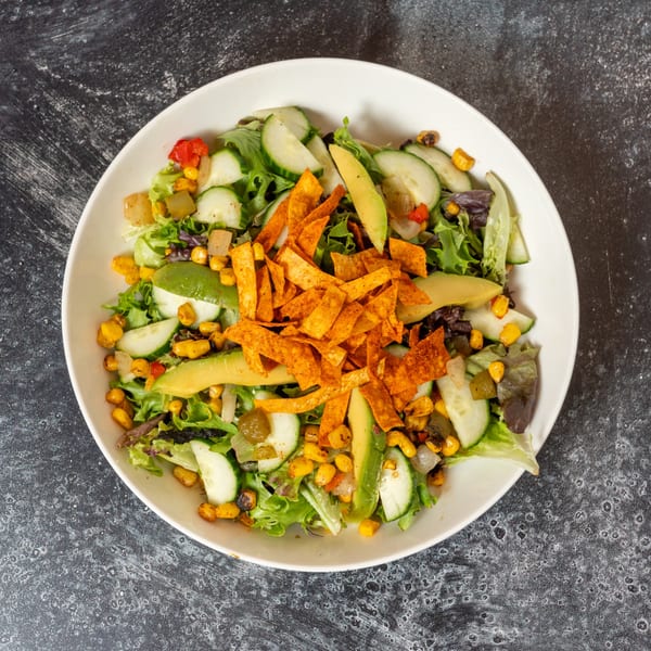 Overhead view of a vibrant salad with lettuce, cucumber, corn, avocado, and tortilla strips in a white bowl.