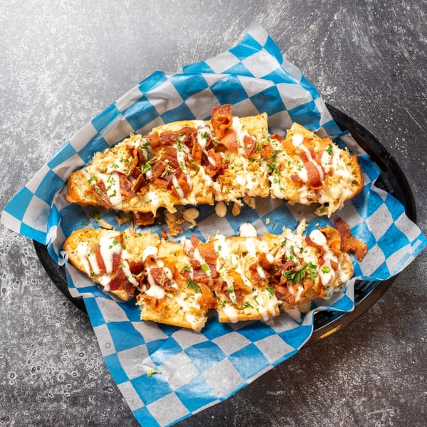 Two halves of cheesy bread topped with bacon, white sauce, and parsley in a basket.