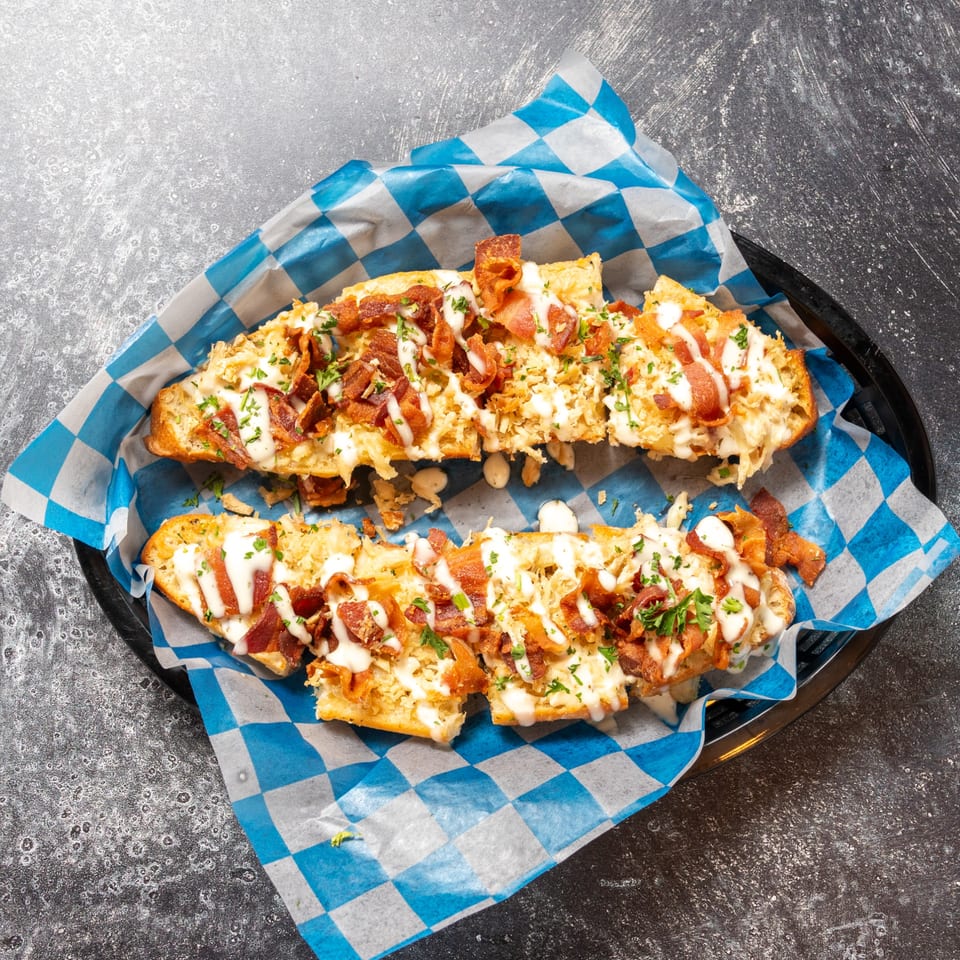Two halves of cheesy bread topped with bacon, white sauce, and parsley in a basket.
