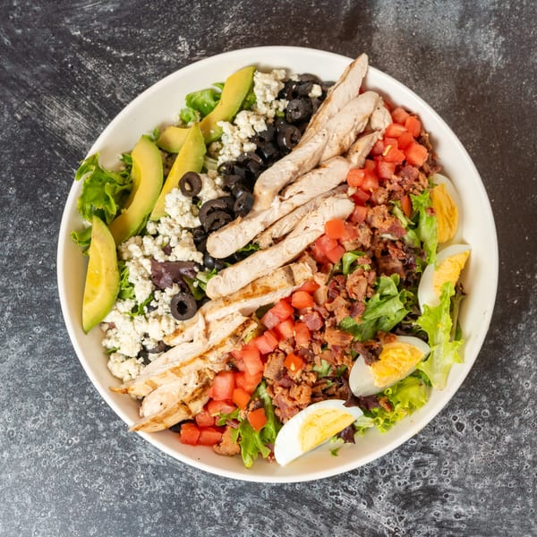 Cobb salad with grilled chicken, avocado, olives, blue cheese, bacon, tomatoes, and hard-boiled eggs.
