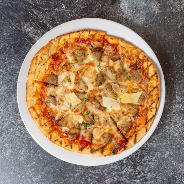 Grilled flatbread pizza with sausage, melted cheese, tomato sauce, and shaved parmesan on a white plate.
