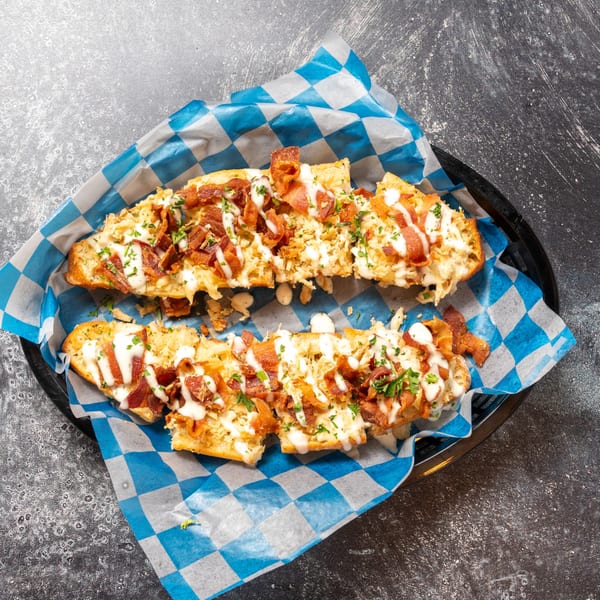 Two halves of cheesy bread topped with bacon, white sauce, and parsley in a basket.