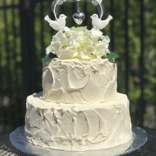 Two-tier white wedding cake with textured frosting, white flowers, and dove cake topper.