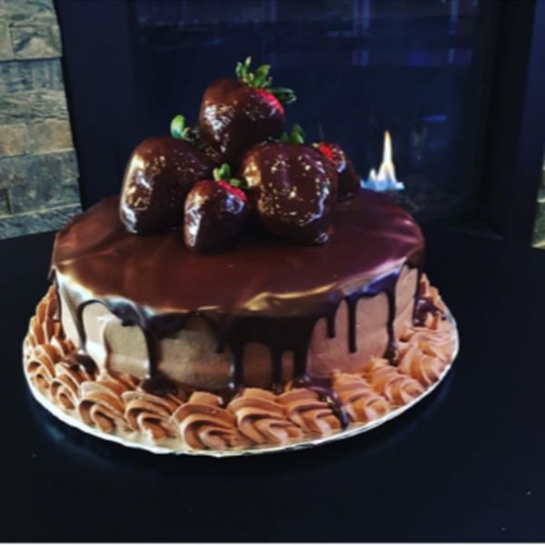 Chocolate cake with chocolate-covered strawberries and a fireplace in the background.