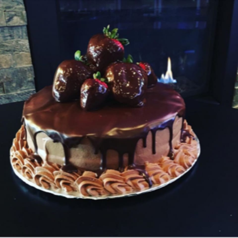 Chocolate cake with chocolate-covered strawberries and a fireplace in the background.